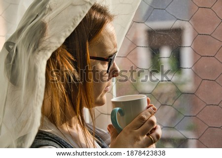 beautiful woman looking out the window melancholy on a rainy afternoon having a coffee or tea. bad weather depression concept