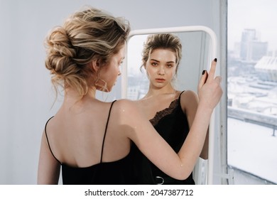 Schöne Frau mit Blick auf Reflection in Mirror Fotografie. Ernsthafte Attraktive Girl Checks Gesichtsbezug und Aussehen im Wohnzimmer. Lady Prepare for Celebrative Party or Dating