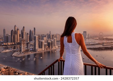 A beautiful woman looks at the panoramic view of the Dubai Marina district during golden sunset time, UAE - Powered by Shutterstock