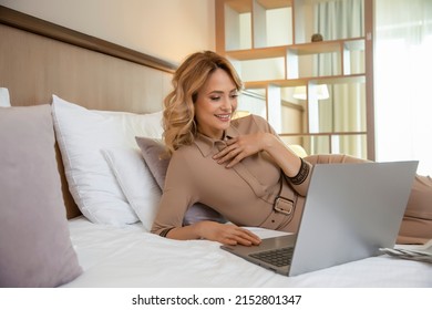 Beautiful woman lying on a hotel bed , dressed, using her notebook