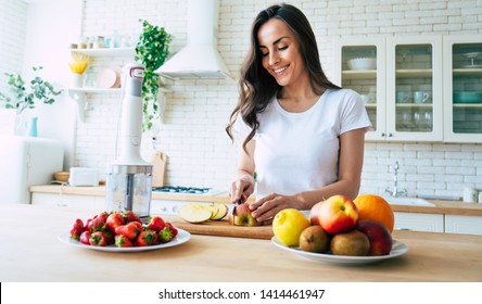 Beautiful woman making fruits smoothies with blender. Healthy eating lifestyle concept portrait of beautiful young woman preparing drink with bananas, strawberry and kiwi at home in kitchen. - Powered by Shutterstock