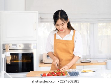 Beautiful woman making fruits tart chopping strawberry. Healthy eating lifestyle concept portrait of beautiful young woman preparing  strawberry and blueberry tart at home in kitchen. - Powered by Shutterstock