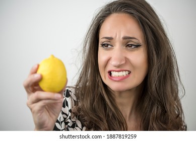 Beautiful woman is making a sour grimace while holding a lemon