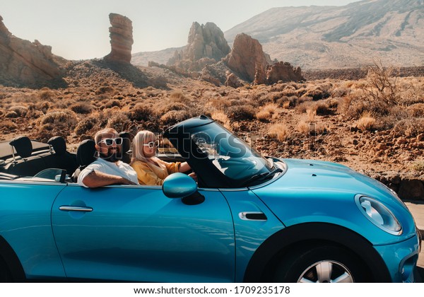 beautiful woman and man in a car trip,\
convertible, volcano crater, sunny\
weather