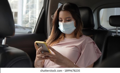 A beautiful woman with a mask to prevent the virus using her cell phone in a car, a passenger wearing a mask and checking her cell phone, on a trip through the city