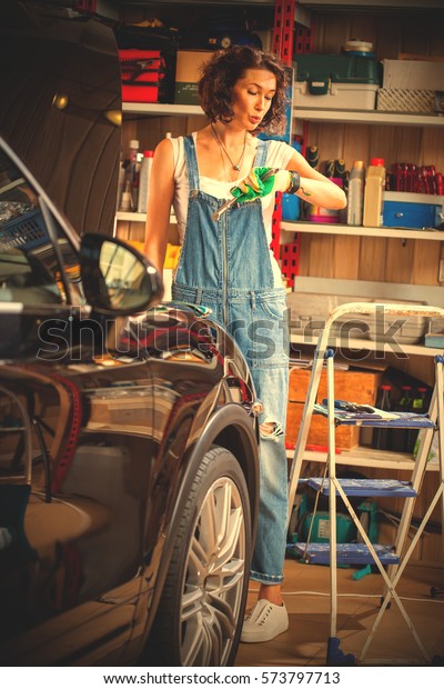 beautiful woman mechanic in blue overalls\
looks at wristwatch. Car body shop in the garage and a female car\
mechanic. instagram image filter retro\
style