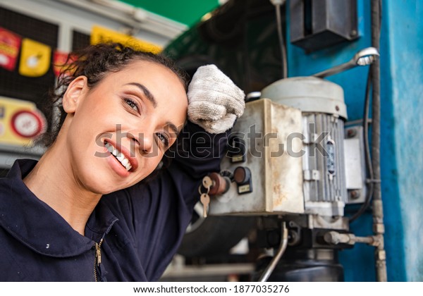 Beautiful woman mechanics in\
uniform relaxing after working in auto service with lifted vehicle\
and reporting. Car repair and maintenance. Maintenance and\
acceptance
