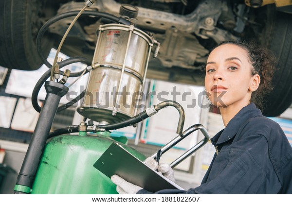 Beautiful woman mechanics in\
uniform is working in auto service with lifted vehicle and paper\
reporting. Car repair and maintenance. Maintenance and\
acceptance