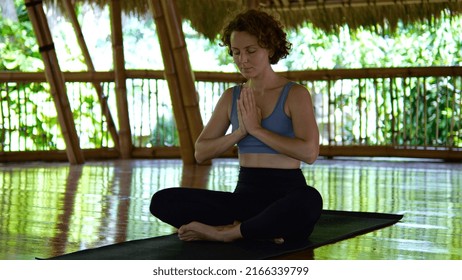 A beautiful woman is meditating on a bamboo terrace with her hands clasped in a namaste gesture. A woman performs spiritual practices for harmony within herself. Prayer to the Buddhist gods.