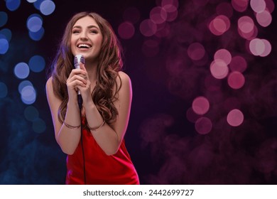 Beautiful woman with microphone singing on stage in color lighted smoke