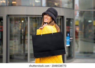 Beautiful woman with mockup black shopping bag in her hands. She stands against the shopping mall. Happy lifestyle and holiday discounts concept.