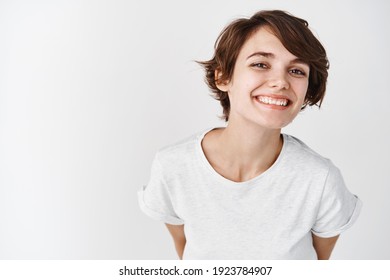 Beautiful woman with natural smooth skin without makeup, posing happy and smiling at camera, standing in t-shirt against white background.