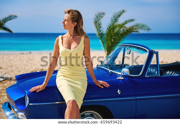 Beautiful woman near retro cabriolet car on the\
tropical beach. Idyllic\
scenery