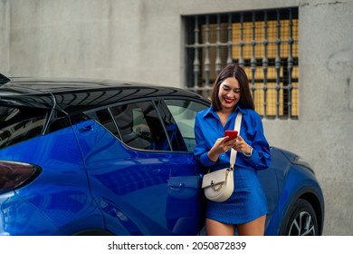 Beautiful Woman Next To Blue Car Using And Looking At Cell Phone