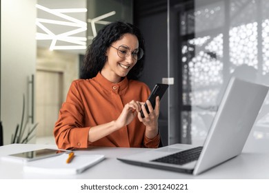 Beautiful woman in the office, happy and smiling latin american business woman uses internet phone close up, female worker reads message and browses internet pages inside office building - Powered by Shutterstock