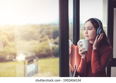 Beautiful woman on a casual day in asia listen to music with headphones. Sip coffee and look out the window at the coffee shop. - Powered by Shutterstock