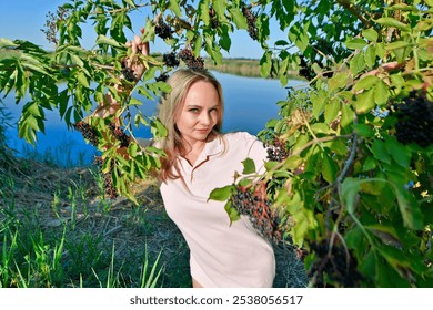 A beautiful woman on the shore of a lake in the branches and clusters of elderberries. - Powered by Shutterstock