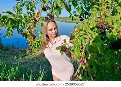 A beautiful woman on the shore of a lake in the branches and clusters of elderberries. - Powered by Shutterstock