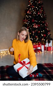 Beautiful woman opening gifts at christmas tree for new year - Shutterstock ID 2395500799