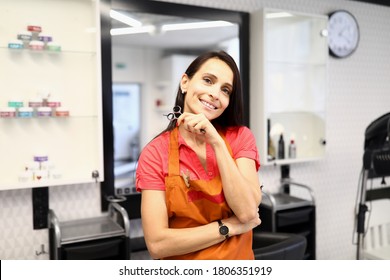 Beautiful woman in orange apron look and smile. Professional hairdresser hold scissors in hand in beauty salon. - Powered by Shutterstock