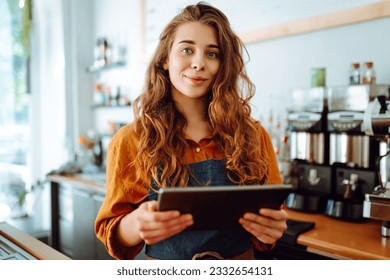 Beautiful woman owner stands behind the counter of a coffee shop. A barista with a digital tablet takes an order. Business concept. Takeaway food. - Powered by Shutterstock