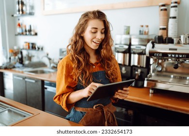 Beautiful woman owner stands behind the counter of a coffee shop. A barista with a digital tablet takes an order. Business concept. Takeaway food. - Powered by Shutterstock