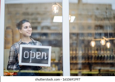 Beautiful Woman Owner Stands And Opens A Wide Sign Through The Shop Window And Smile. Small Business, Grocery Store, Prevent, Minimise, Reuse And Recycle Waste Concept.