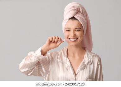 Beautiful woman in pajamas brushing teeth on light background - Powered by Shutterstock