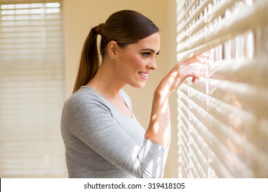 beautiful woman peeking through window blinds 