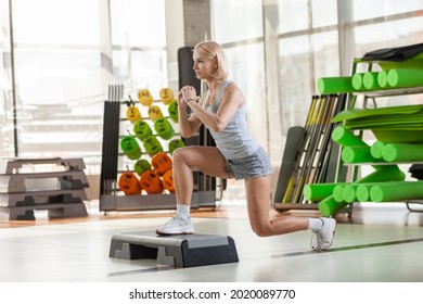 Beautiful woman with perfect body doing lunges exercises on the stair stepper in the gym. Intense aerobics. Healthy lifestyle concept.