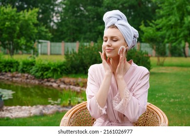 Beautiful woman with perfect skin doing makeup and cleansing skin on her face with cotton pillow after shower in towel on her head while sitting in chair garden at home in fresh air Skin care concept - Powered by Shutterstock