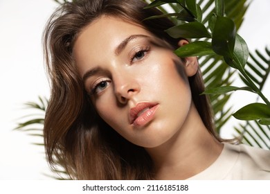 Hermosa mujer con piel perfecta y maquillaje natural sosteniendo tropicales   hojas