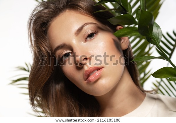 Beautiful woman with perfect  skin and natural\
make-up holding tropical  \
leaves