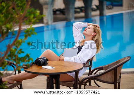 Beautiful woman photographer blogger on vacation, working with laptop by the pool. Freelance remote work