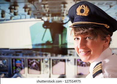 Beautiful woman pilot wearing uniform with epaulets, hat with golden wings sitting inside airliner with visible cockpit during flight.
