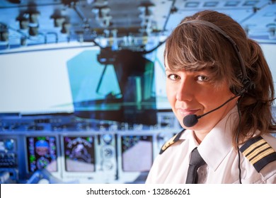 Beautiful woman pilot wearing uniform with epauletes, headset sitting inside airliner with visible cockpit during flight.