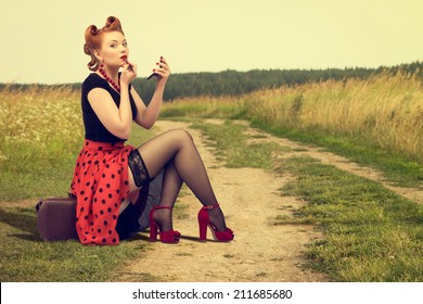 Beautiful Woman In Pin Up Sitting On The Side Of A Rural Road Painting Lipstick.