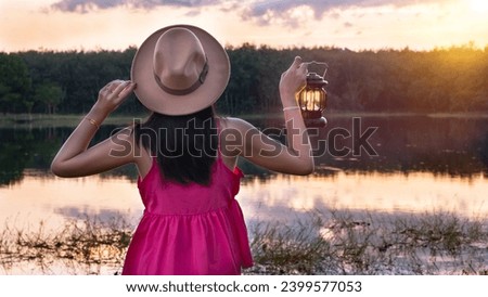 Beautiful woman in pink dress wear a hat holding a lantern in a forest with blurred glowings, Woman holding the lamp outdoors, Hand holds a lamp in the dark, Lantern in twilight sky.