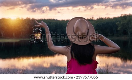 Beautiful woman in pink dress wear a hat holding a lantern in a forest with blurred glowings, Woman holding the lamp outdoors, Hand holds a lamp in the dark, Lantern in twilight sky.