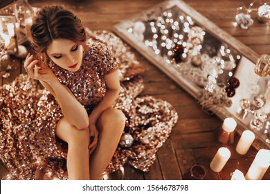 Beautiful Woman In Pink Gold Elegant Sequin Dress Stands Warm Cozy Magic Evening In Luxury Old Christmas Living Room Fairy Tale Interior Design, Decorated By Lights, Candle, Lantern, Garland Light