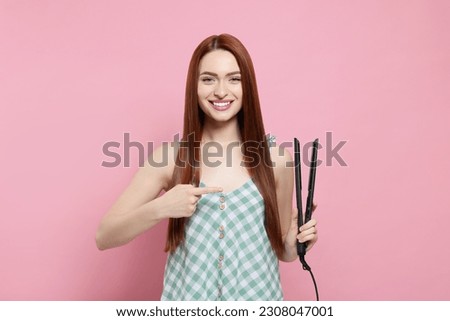 Beautiful woman pointing at hair iron on pink background
