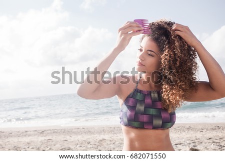Beautiful woman portrait combing her gorgeous curly hair on the beach