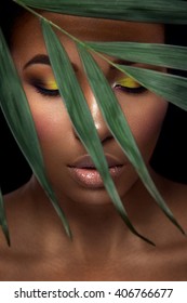 Beautiful Woman Portrait On Black Background. Young Afro Girl Posing With Green Leaves And  Closed Eyes. Gorgeous Make Up. Pure Skin