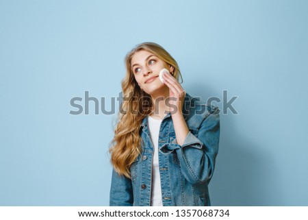 Beautiful woman portrait using cotton swab and thinks about something on a blue background