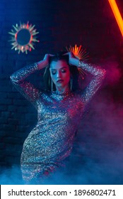 Beautiful woman posing, dancing in colorful bright neon uv blue and red lights. Model wearing luxury earrings, sequin dress
