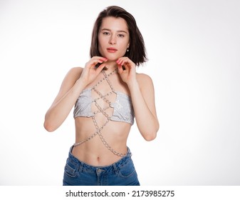 A beautiful woman posing in a jewelry bra with chains and blue jeans isolated on white background. Mockup for party or dance concept with space for text