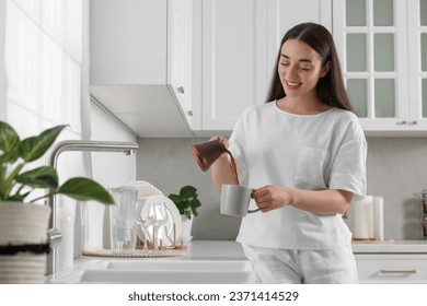 Beautiful woman pouring coffee from jezve into cup in kitchen. Lazy morning