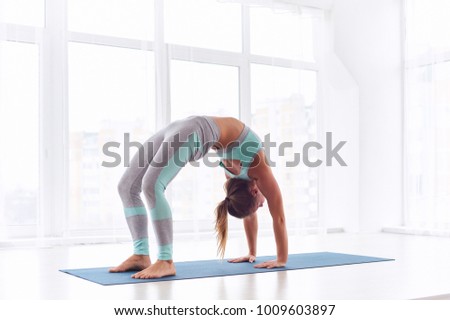 Beautiful woman practices backbend yoga asana Urdhva Dhanurasana - Upward facing bow pose at the yoga studio