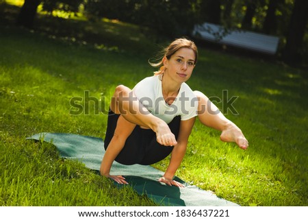 Beautiful woman practices handstand yoga asana Tittibhasana - firefly pose in park.