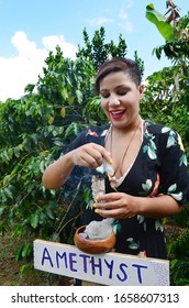 Beautiful woman practicing magic. Witch using sage and healing crystals in nature. Forest witch on a coffee farm in Puerto Rico. Hispanic woman outside with burning sage. Crystal healing, sage cleanse